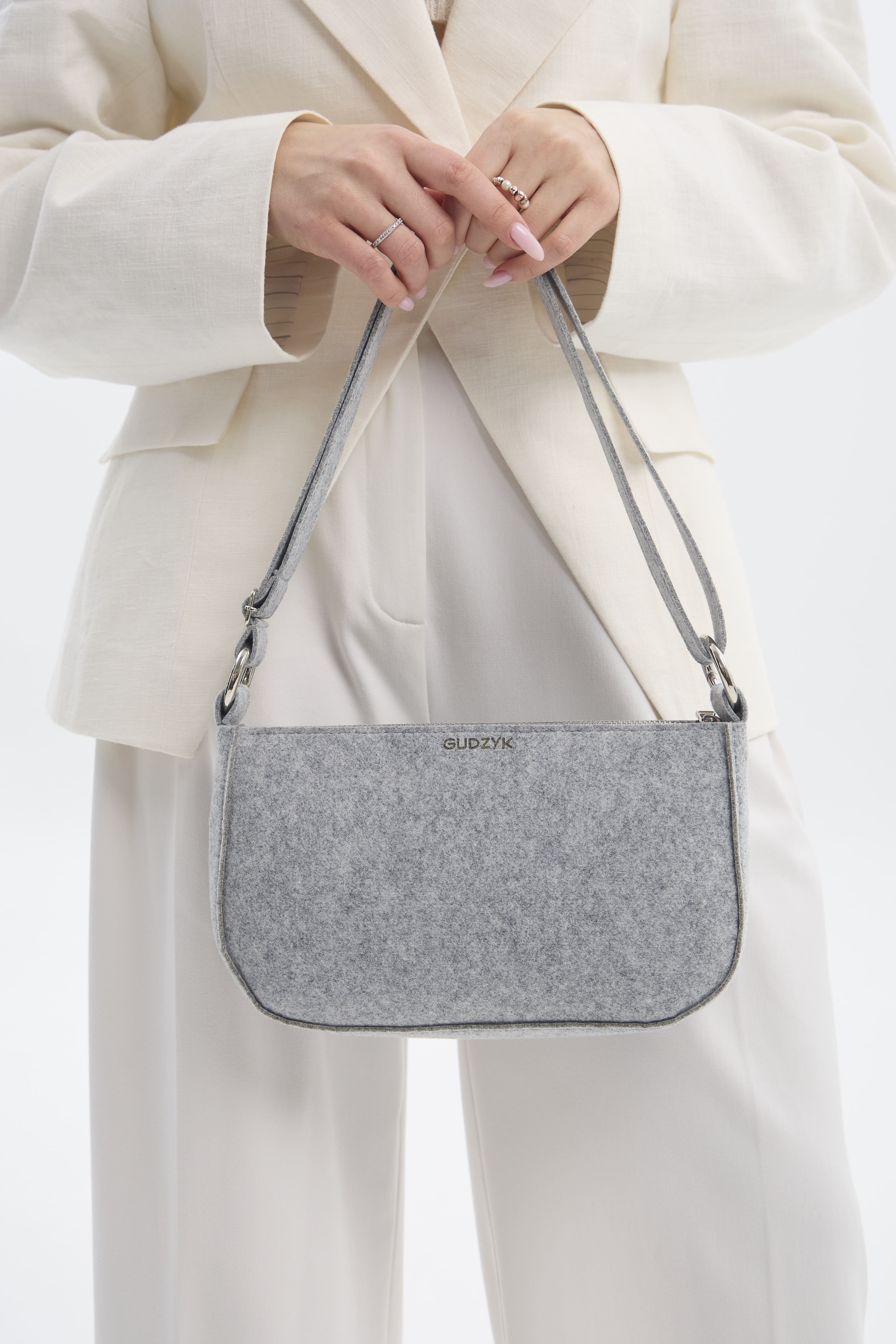 Person holding a gray shoulder bag with a visible brand logo against a white background
