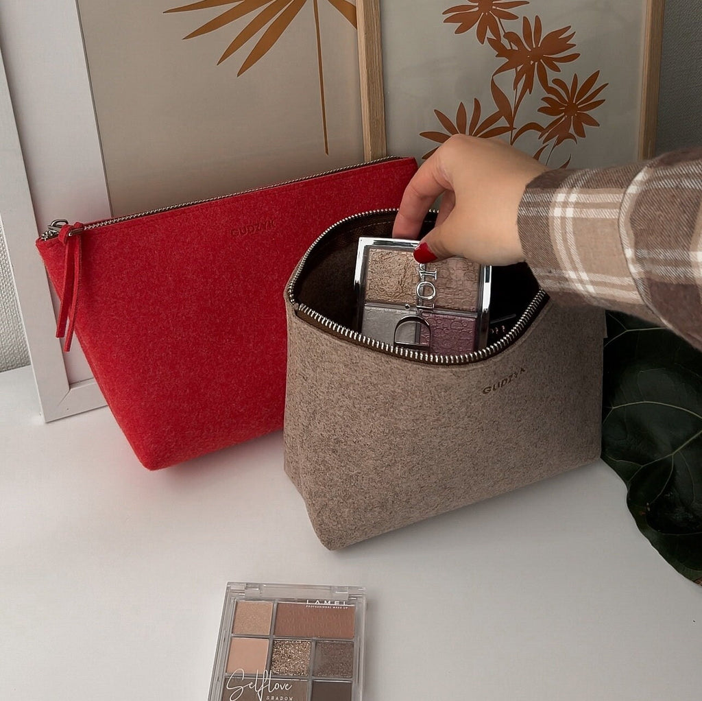 Person opening a beige makeup bag with a red pouch in the background