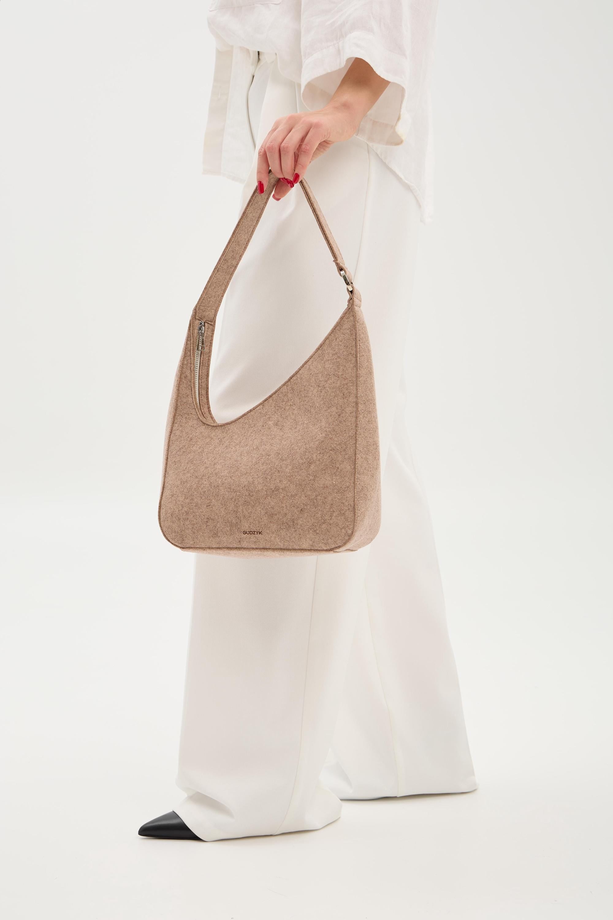 Person holding a beige shoulder bag against a white background