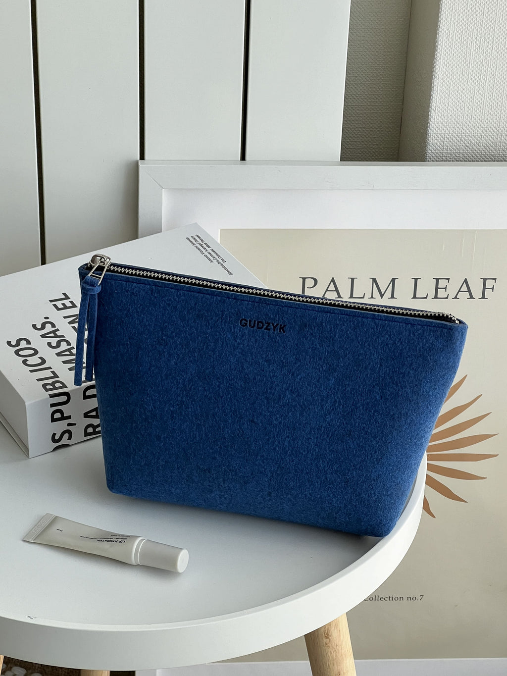 dark blue pouch on a white surface with books and a tube of cream in the background