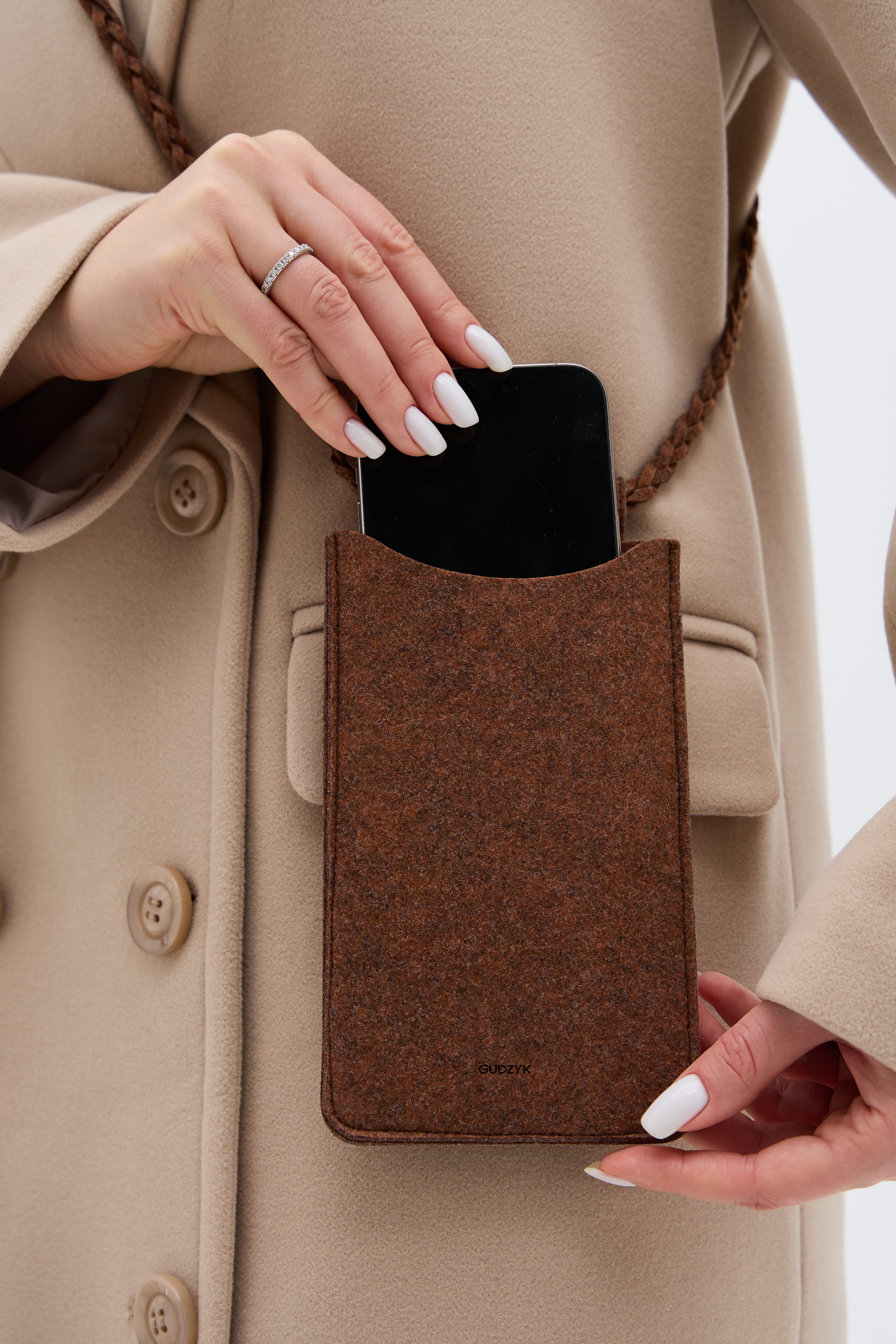 Person holding a brown phone case with a beige coat
