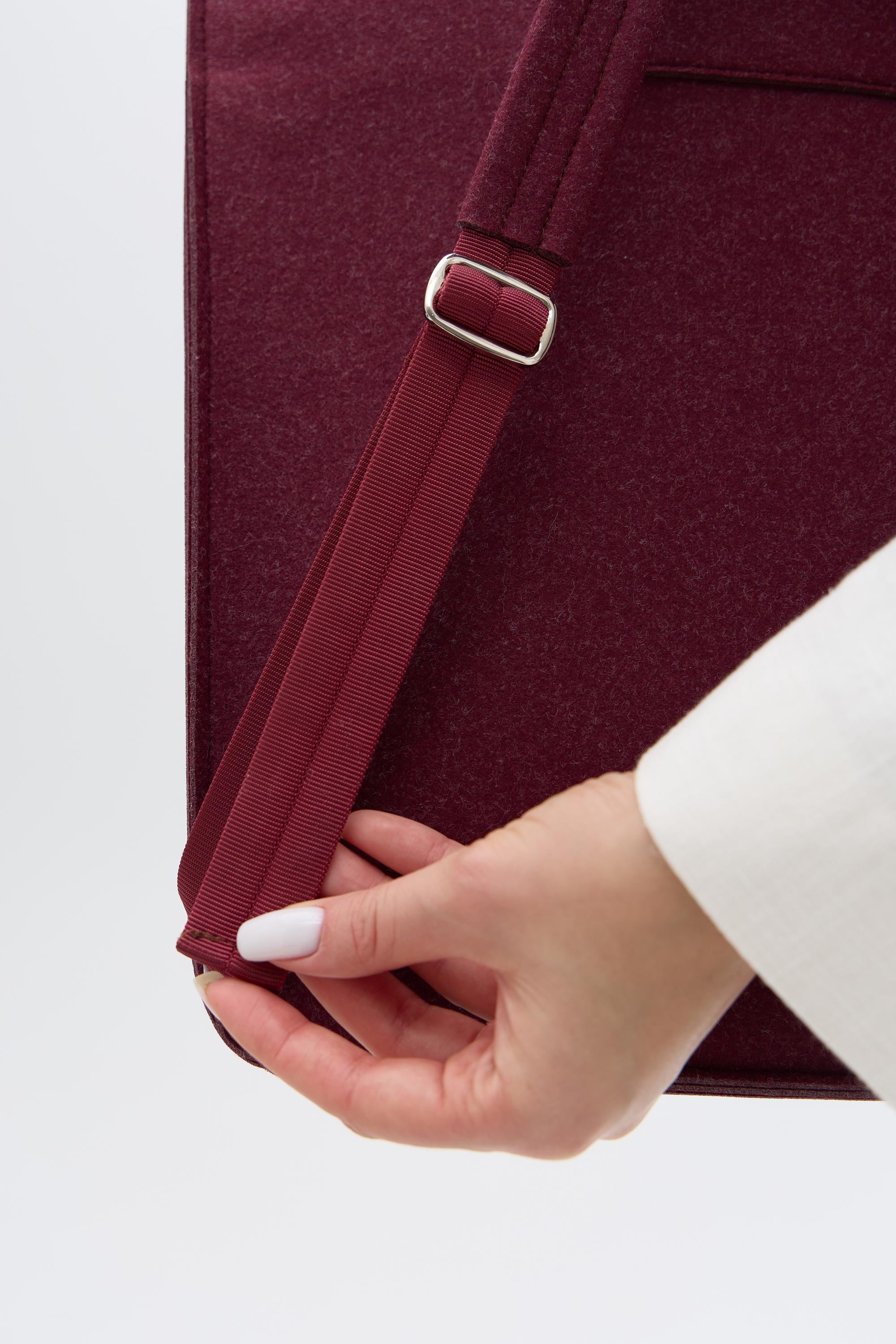 Close-up of a hand adjusting a strap on a burgundy backpack against a white background