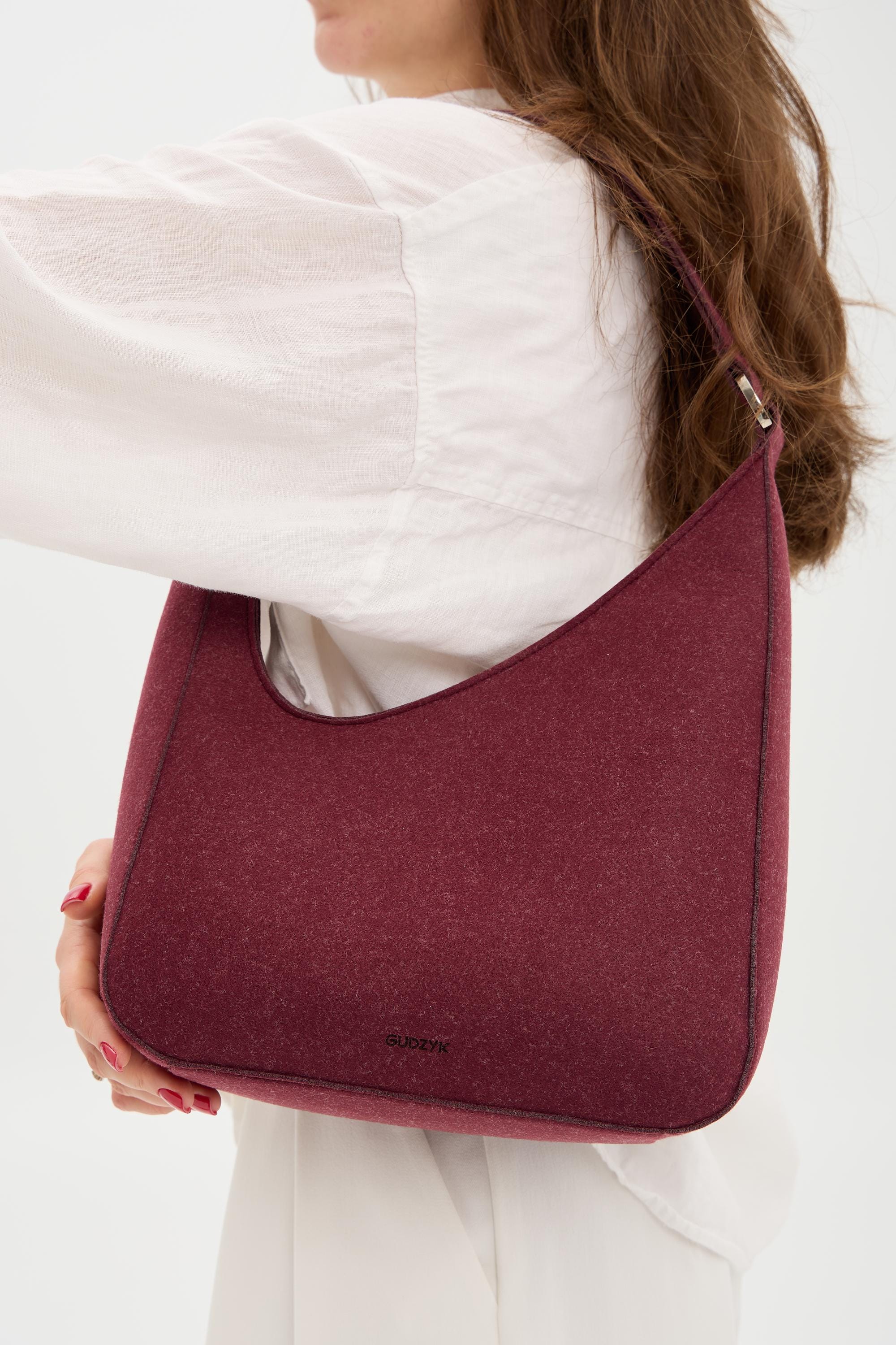 Person holding a burgundy shoulder bag against a white background
