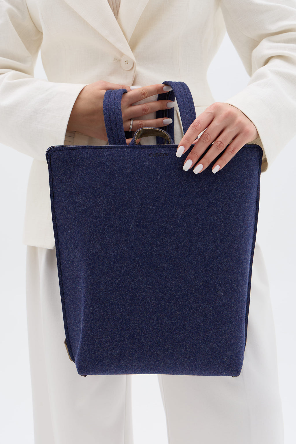 Navy blue backpack held by a person wearing a white outfit