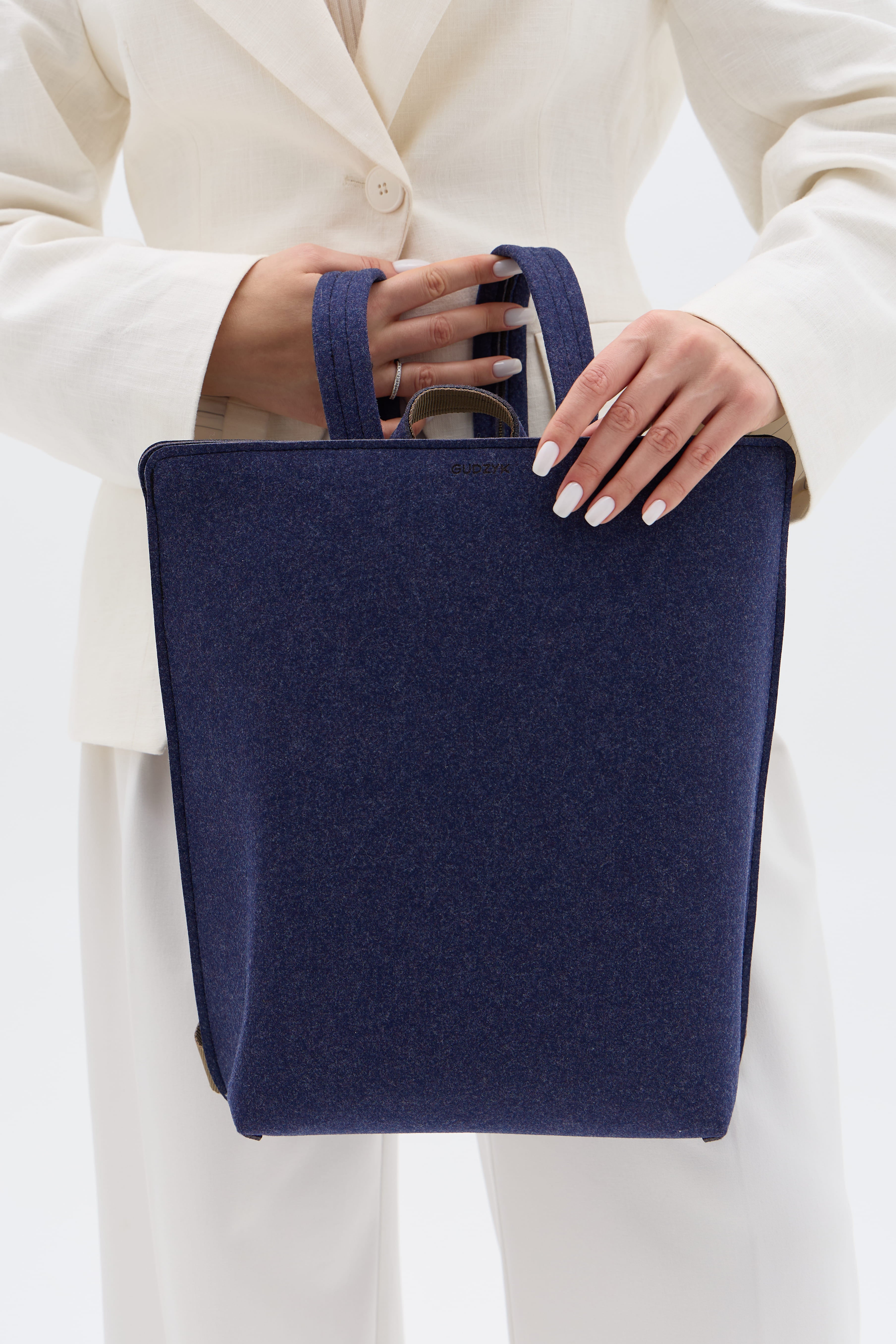 Navy blue backpack held by a person wearing a white outfit