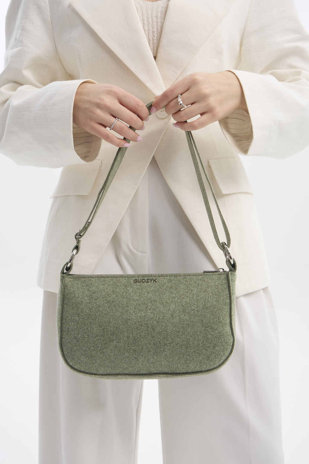 Person wearing a white outfit with a green handbag on a plain background